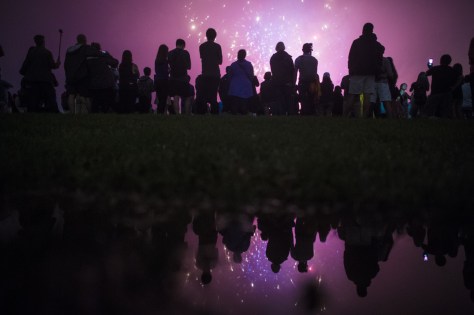 Patrons, reflected in a rain puddle, watch near the Washington Monument as the Independence Day fireworks go off on the National Mall on Monday, July 04. Getty
